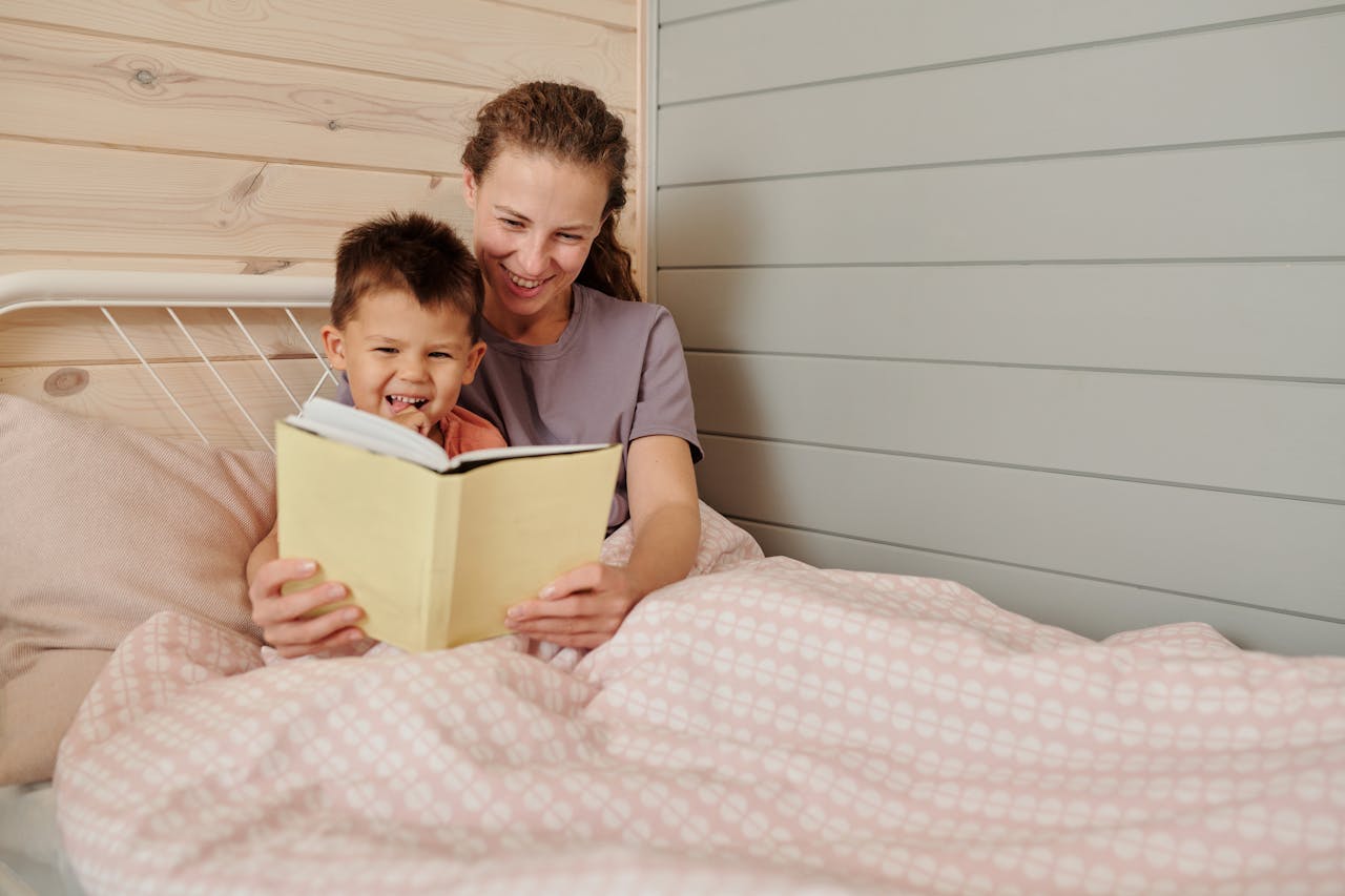 A joyful mother and son bonding while reading a book together in a cozy bedroom setting.